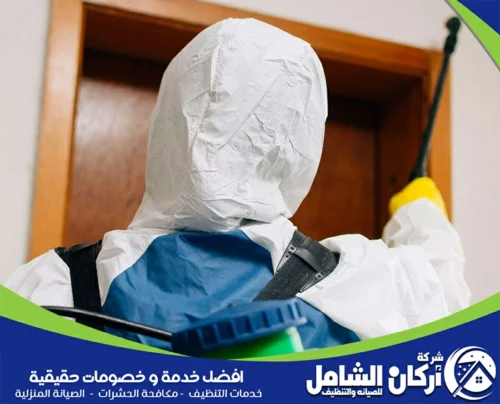 شخص يرتدي ملابس حماية يقوم برش مادة معالجة على السقف داخل غرفة، مع التركيز على التفاصيل لضمان الوصول إلى كل الزوايا.
